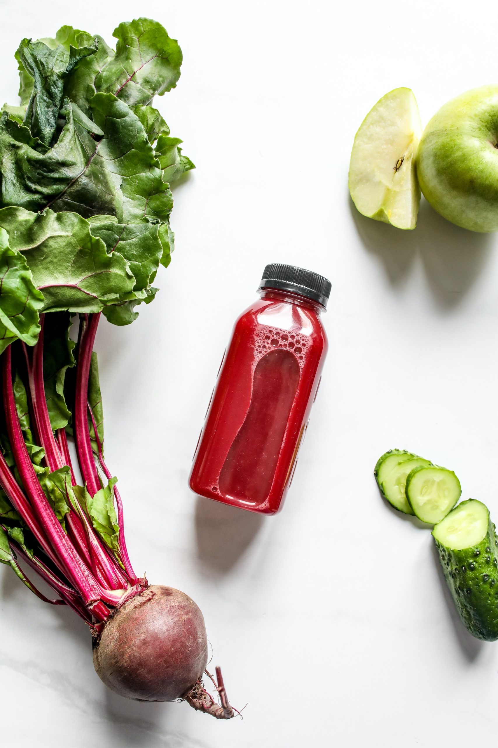 Red Juice in Bottle Beside Beetroot, Apple and Sliced Cucumber